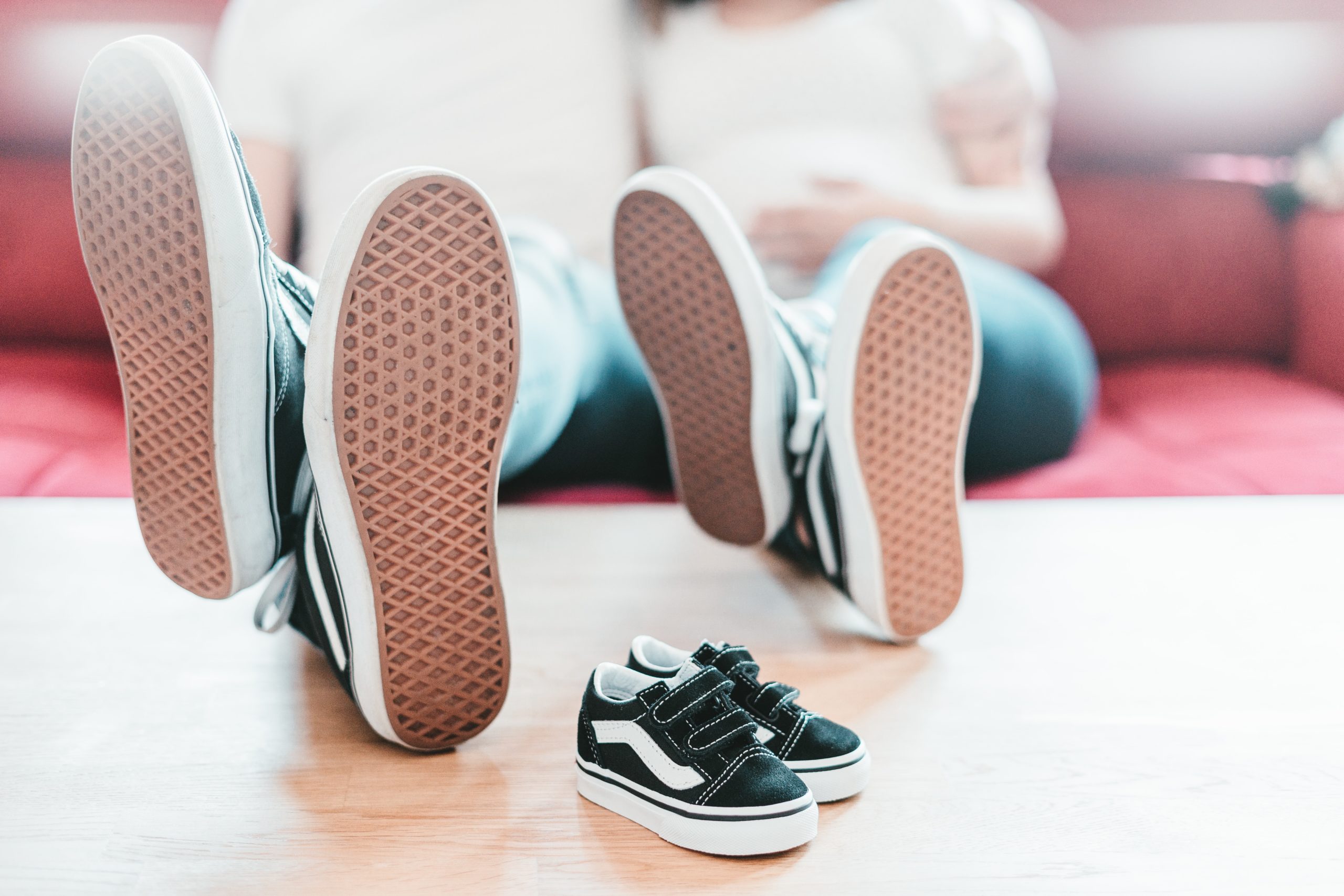 2 parents sitting on a coach announcing pregnancy with a tiny pair of matching shoes