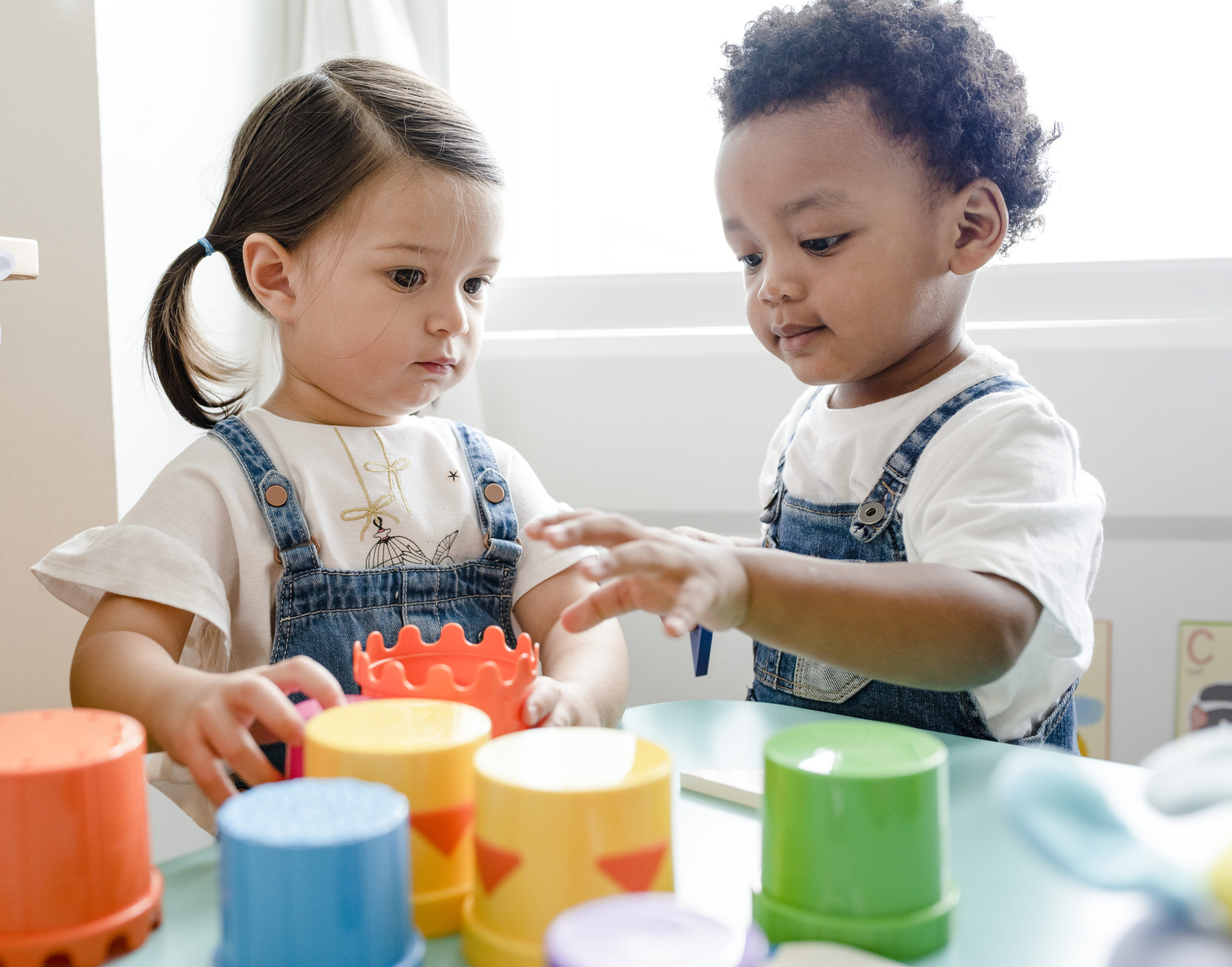 two toddlers playing with colorful cups at daycare.