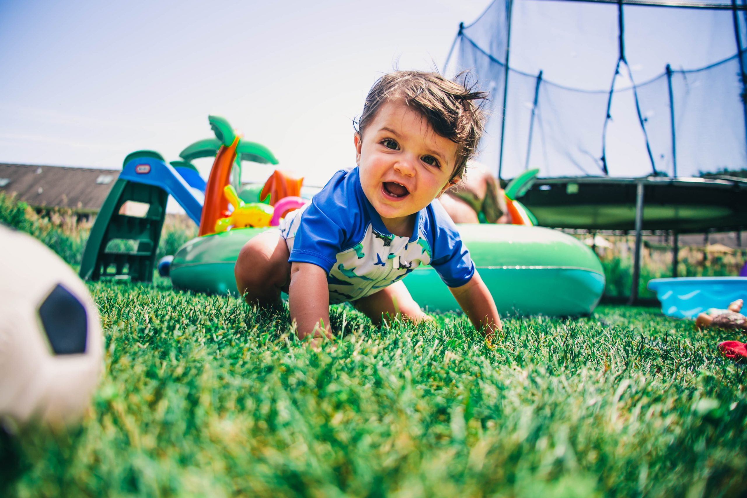 kid crawling in the grass with inner tubes and summer toys around them