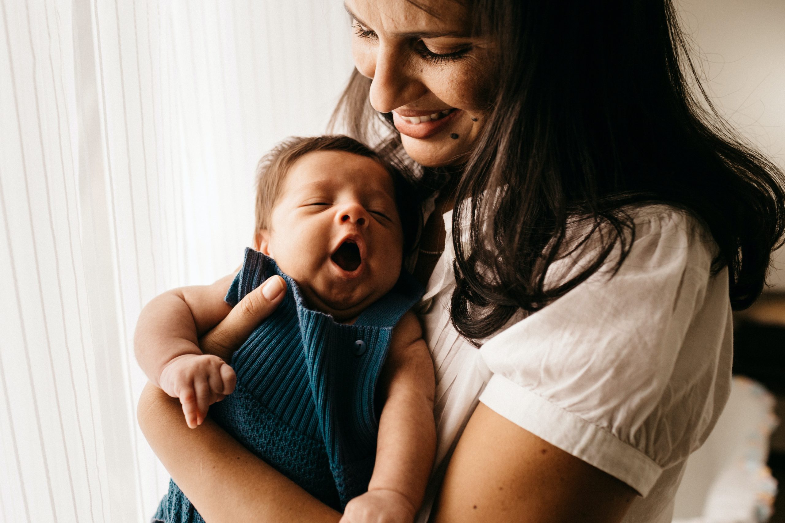 parent smiling while holding baby who is yawning