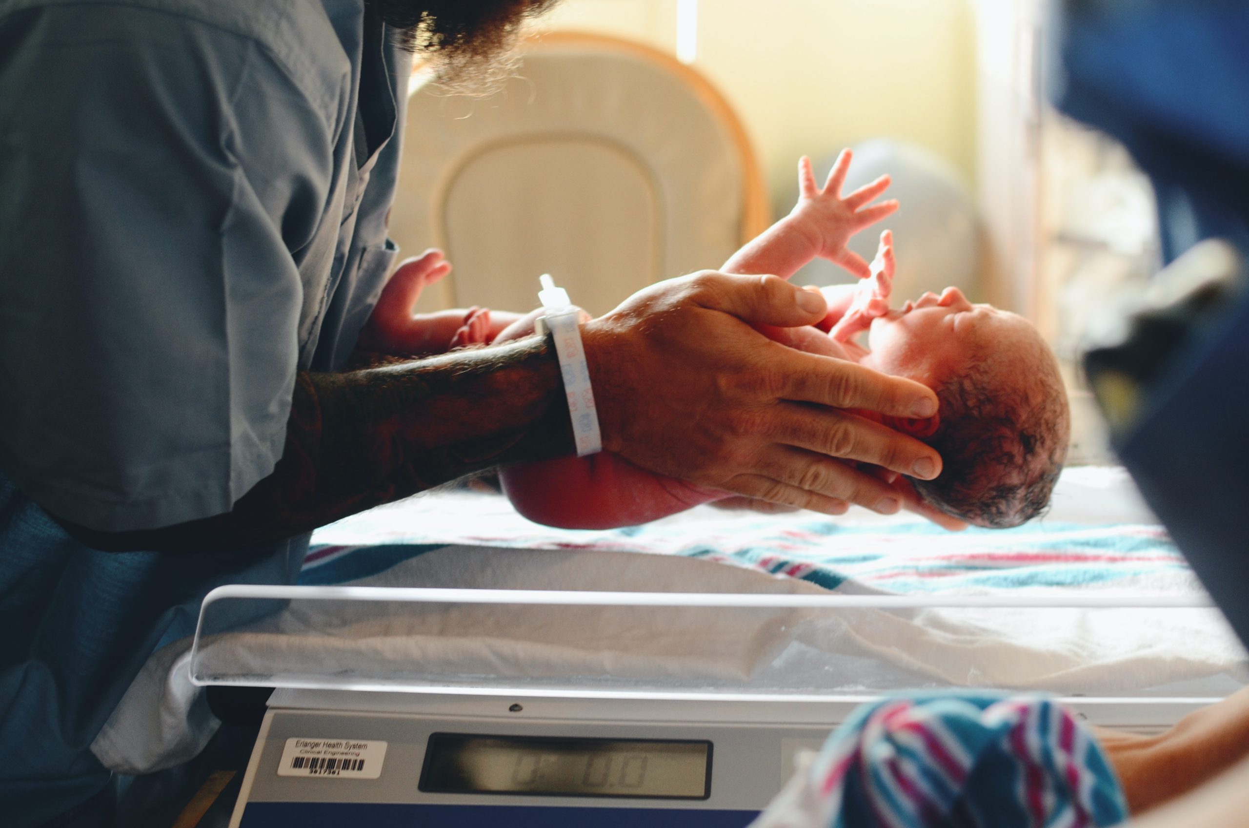 parent holding newborn baby over scale at hospital