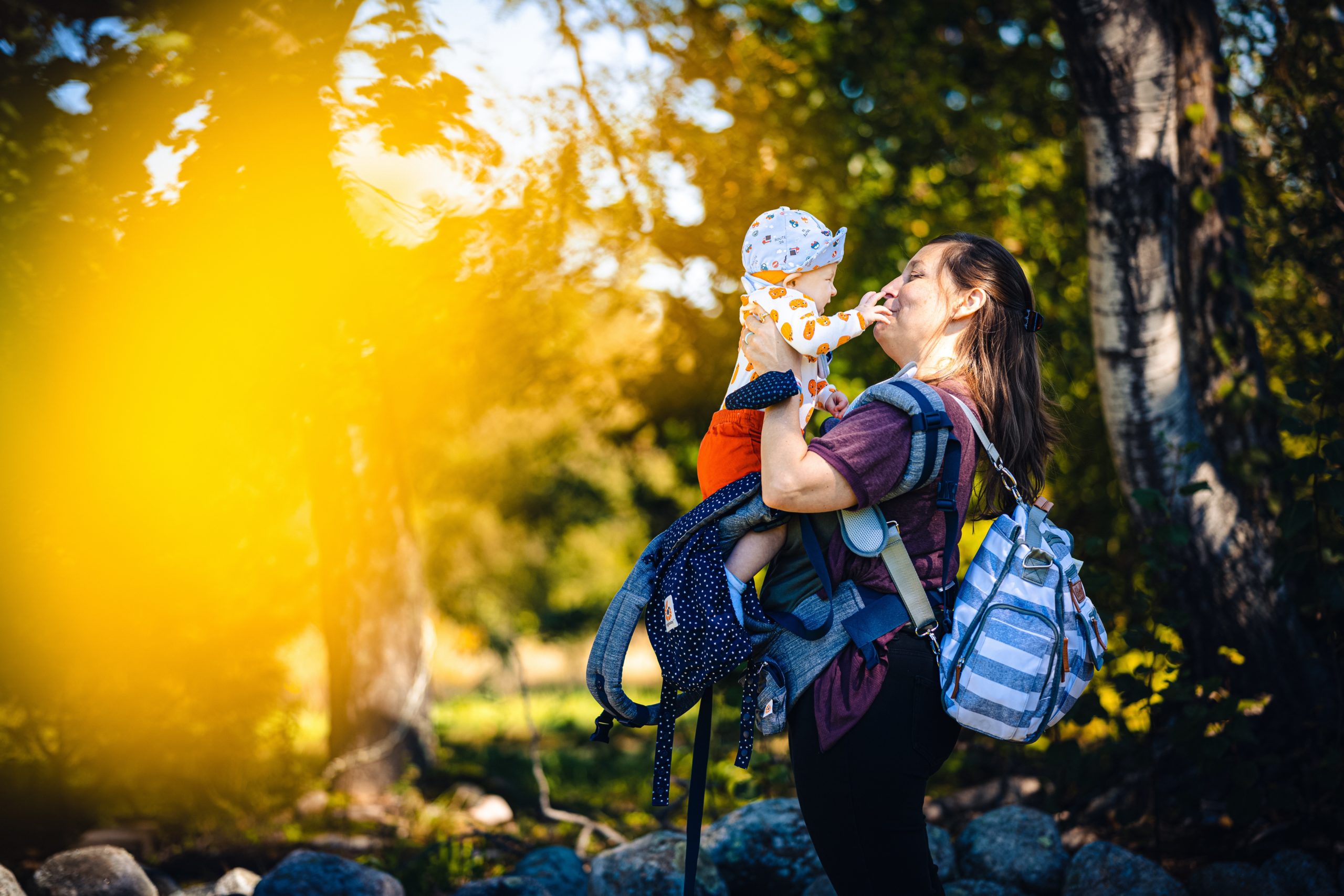 parent wearing baby carrier in the woods and holding baby up to their face.