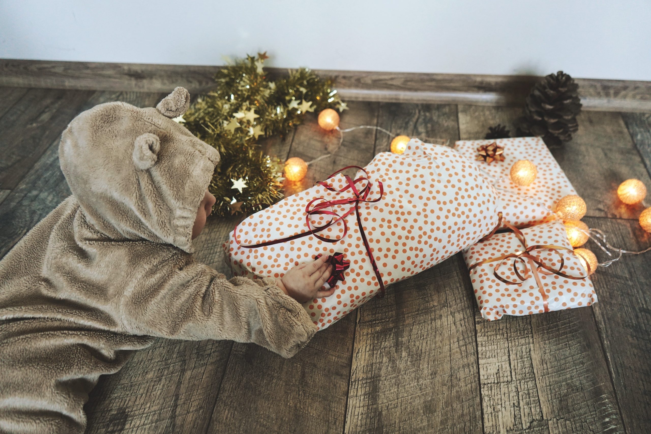 Baby wearing furry onesie, grabbing at wrapped presents on the floor.