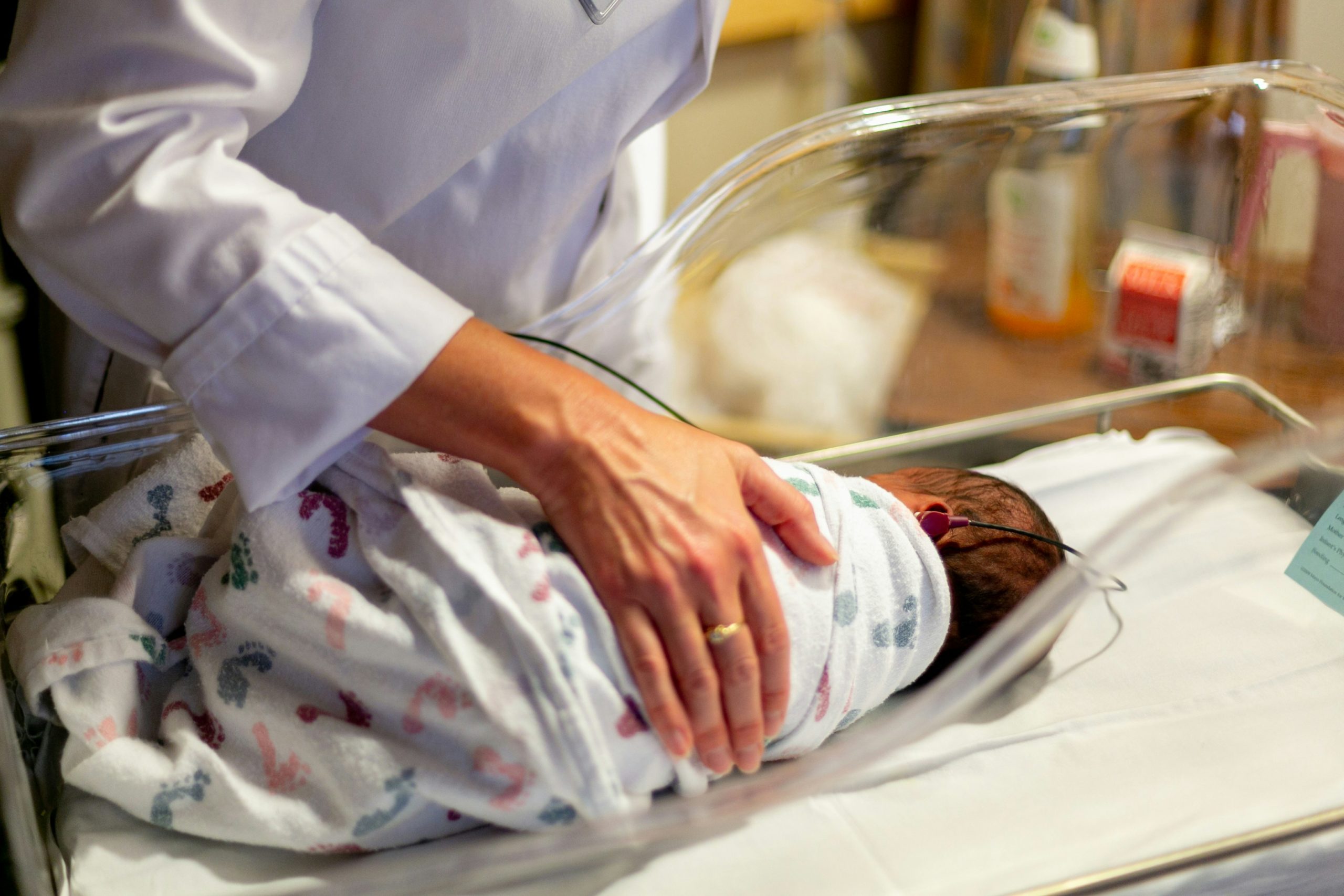 hand of pediatrician on newborn baby who is in a bassinet