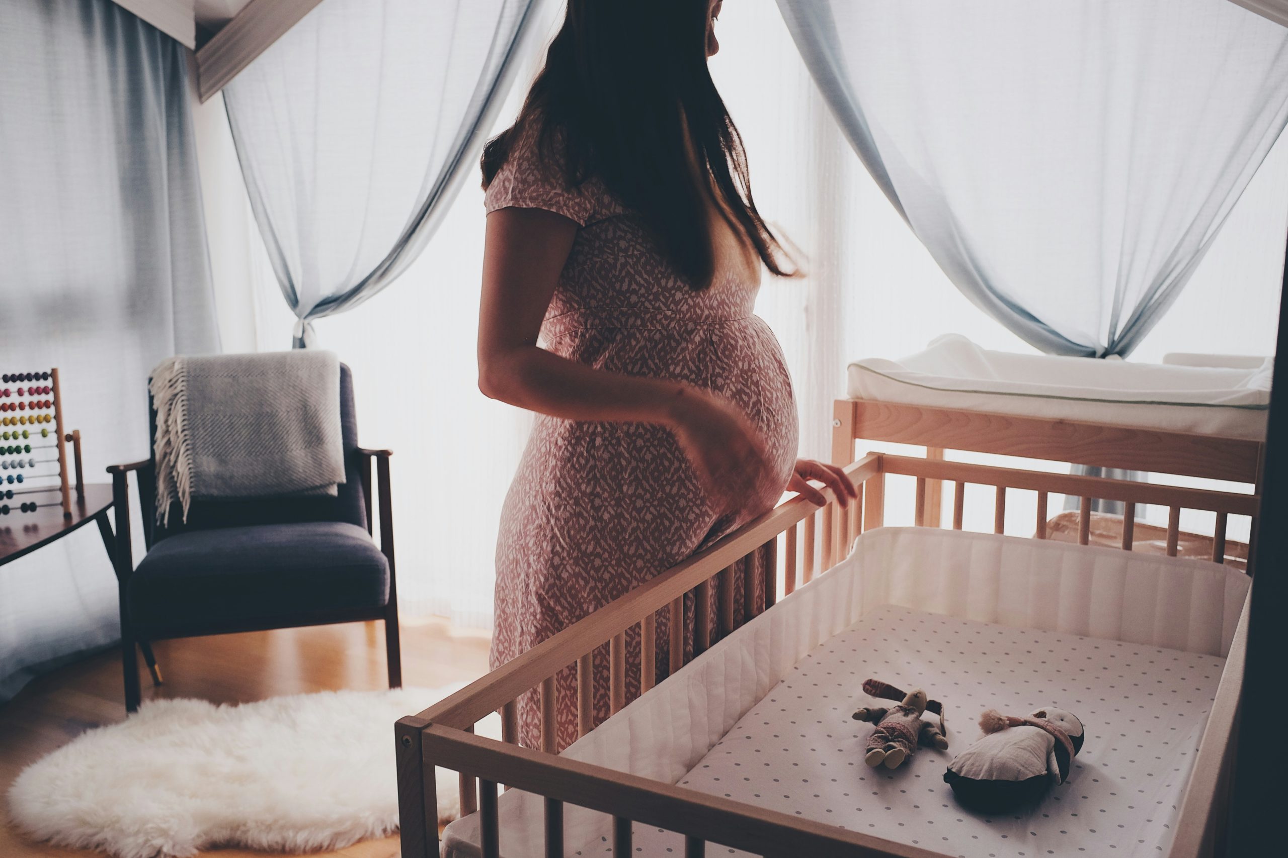 Pregnant parent standing in baby nursery, looking into the crib.