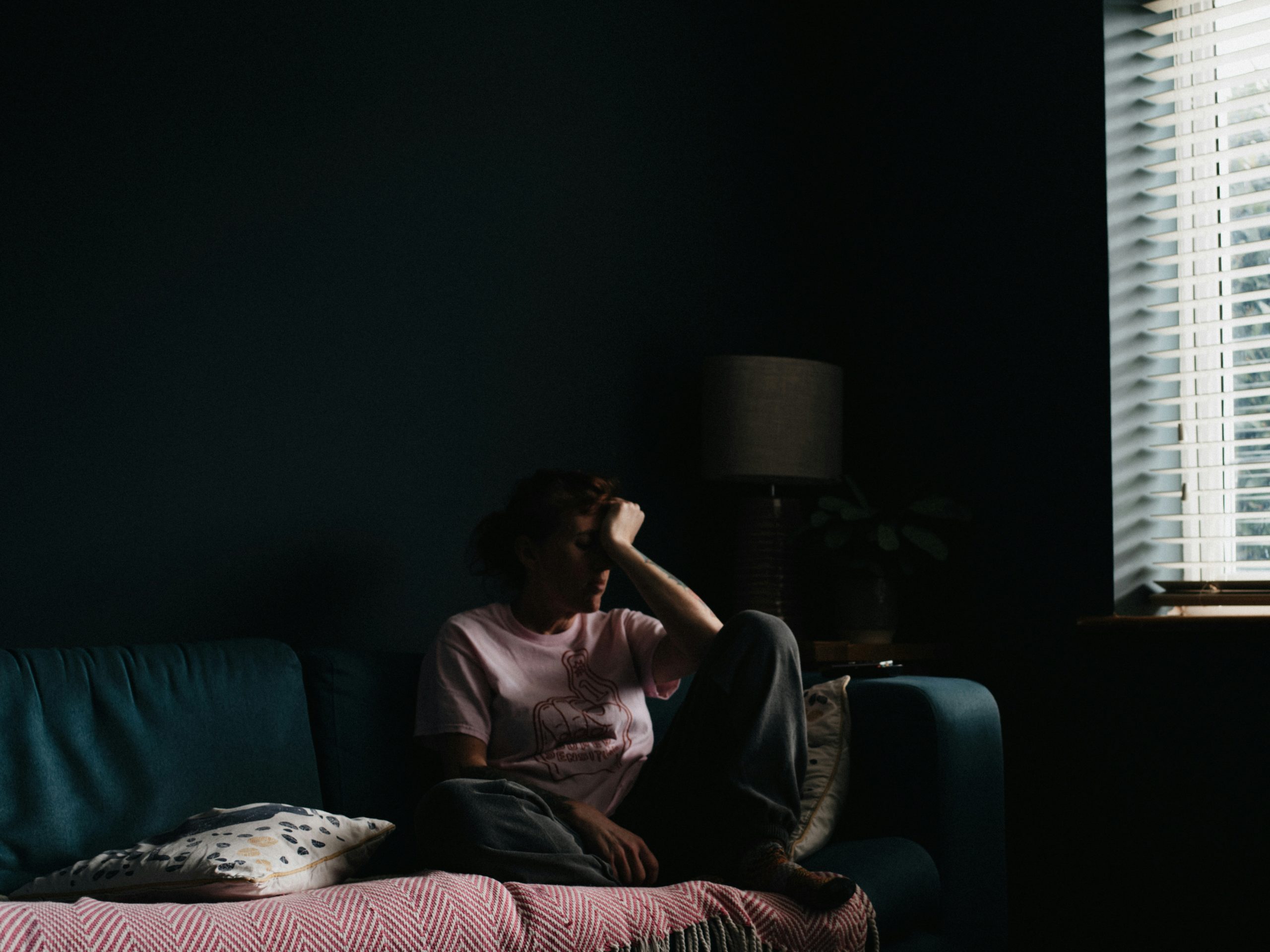 Person sitting on a couch in a dark room with their head in their hands.