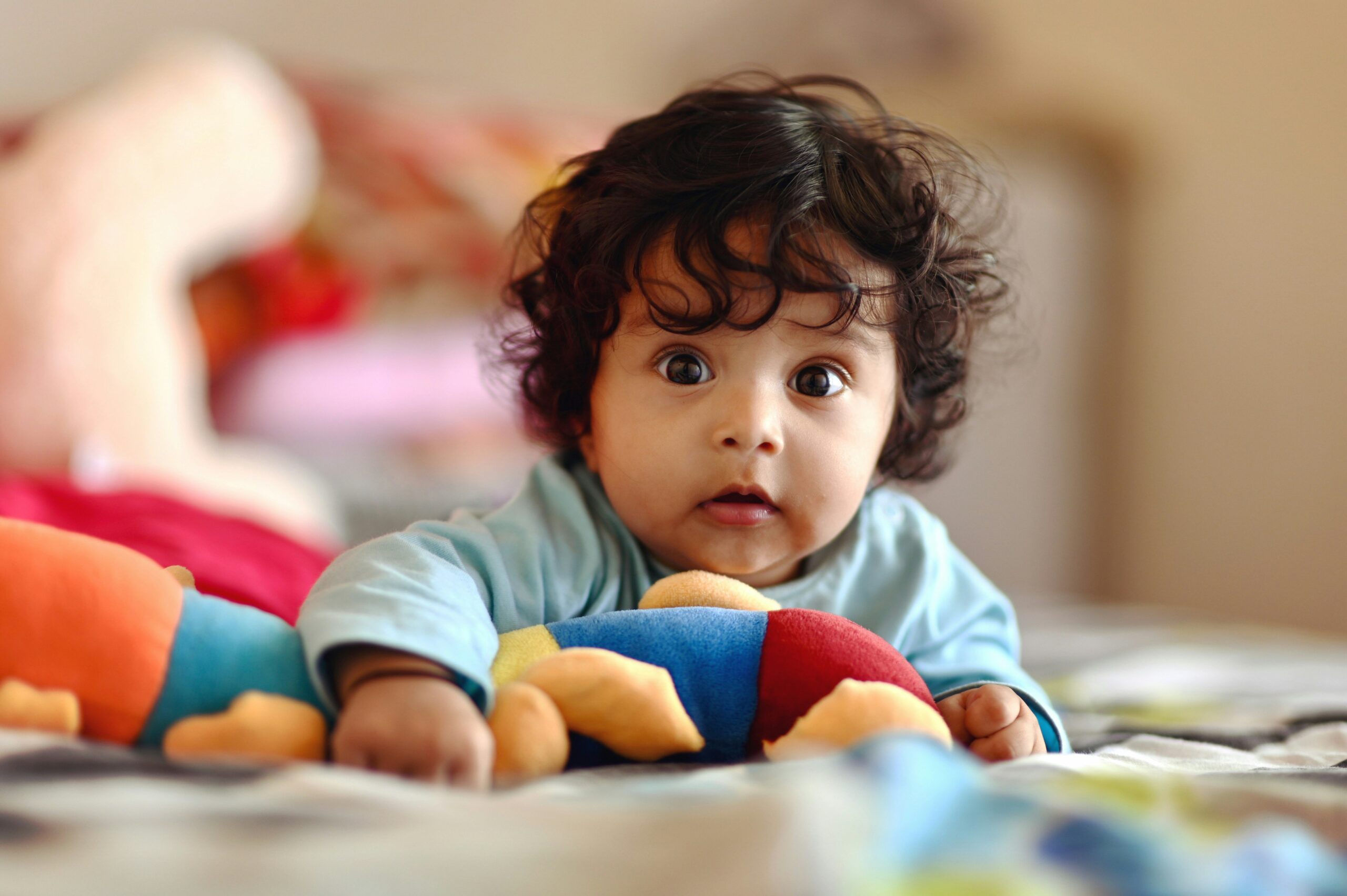 Baby looking directly at the camera while in tummy time with a stuffie under their chest.