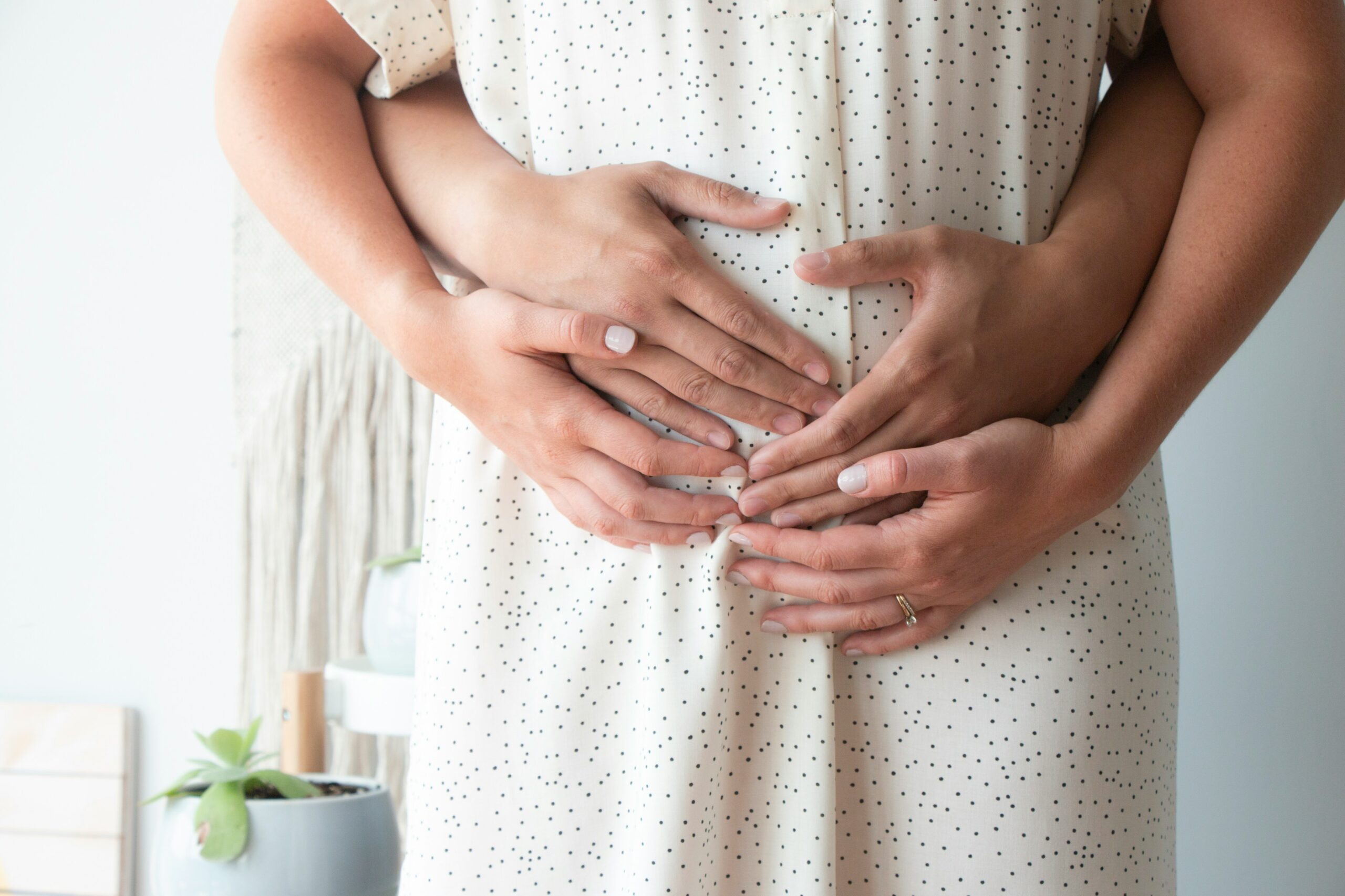 Pregnant person holding their pregnant belly with partner holding them, too.