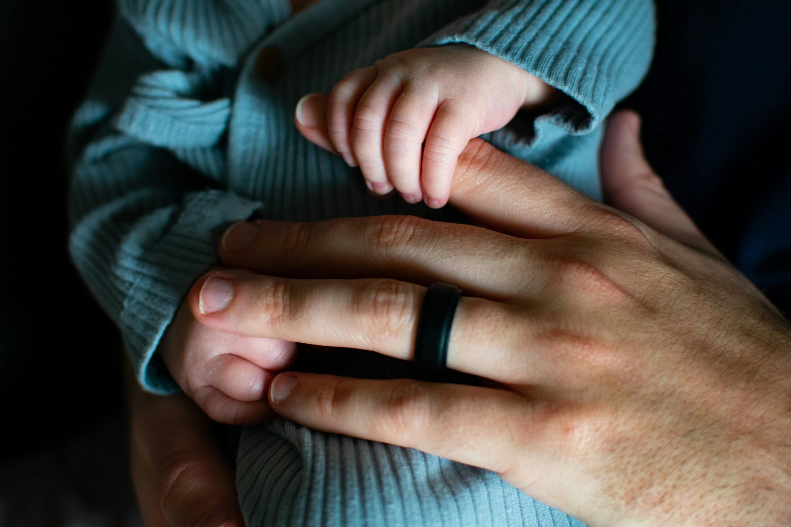 Partner's hand holding baby's hands.