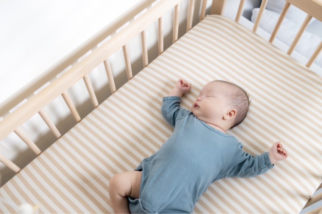Baby sleeping on their back in a crib on a stripped, fitted sheet.