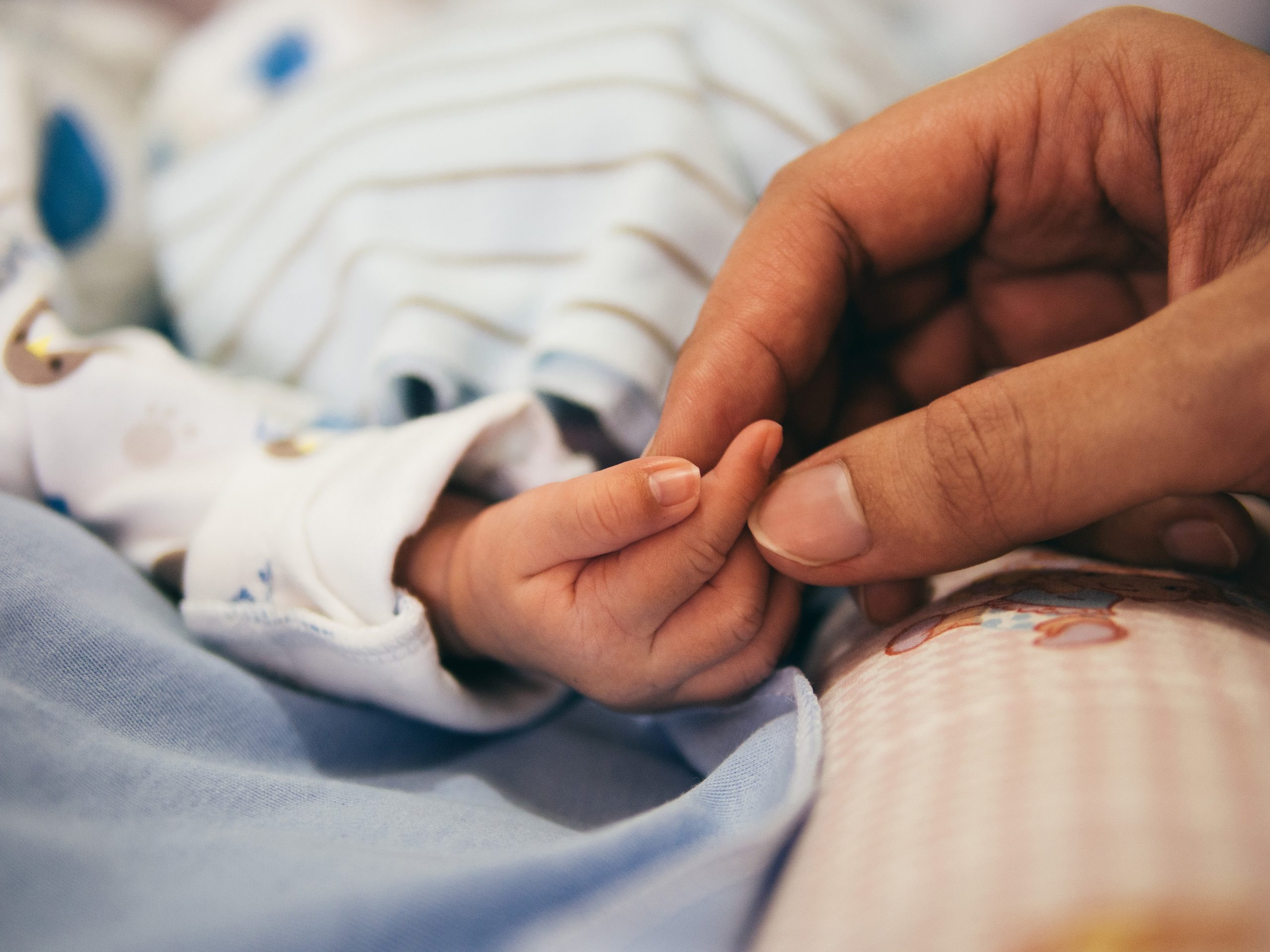 Doula's hand holding the fingers of a newborn's hand.