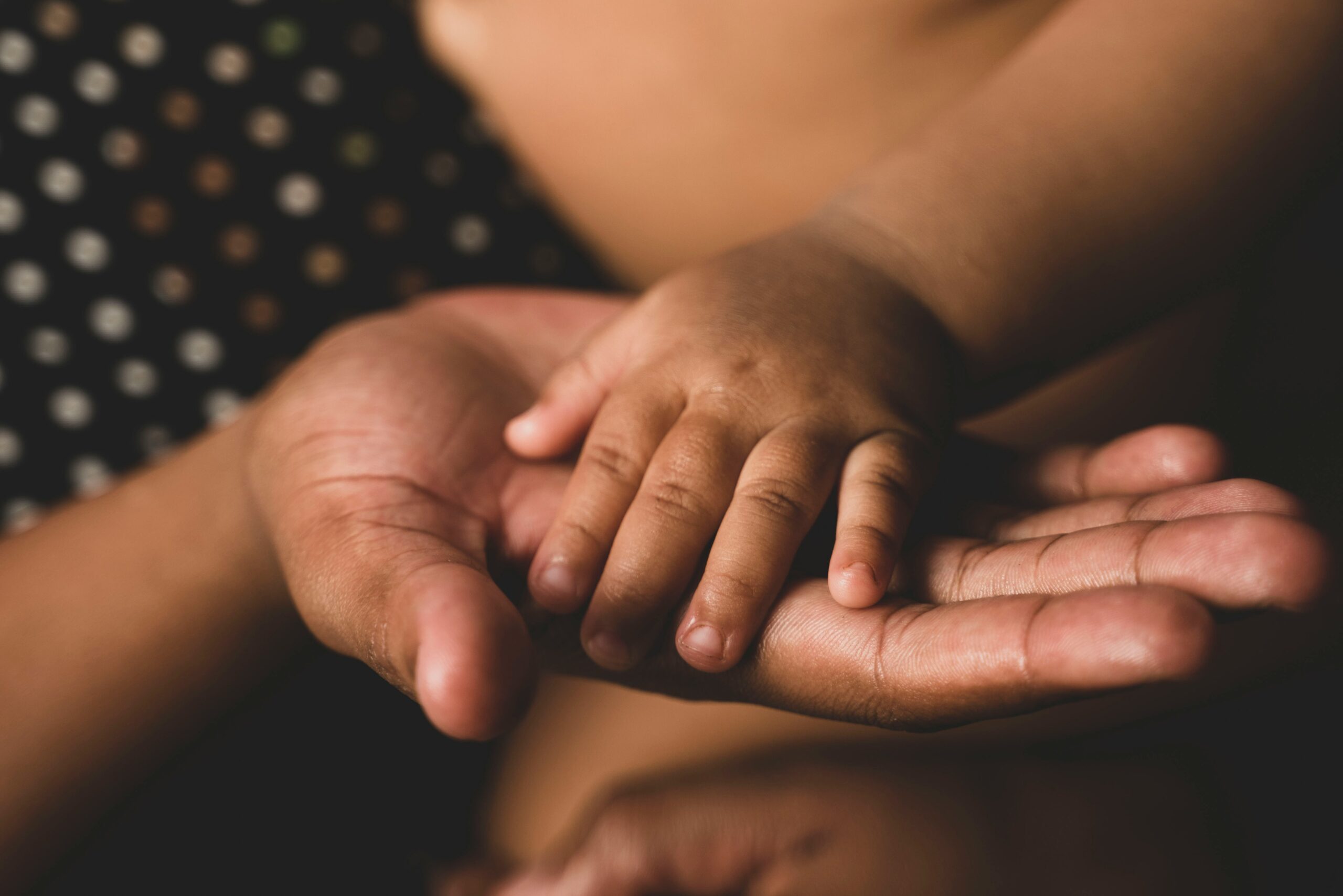 A parent's hand open and holding a baby's hand.