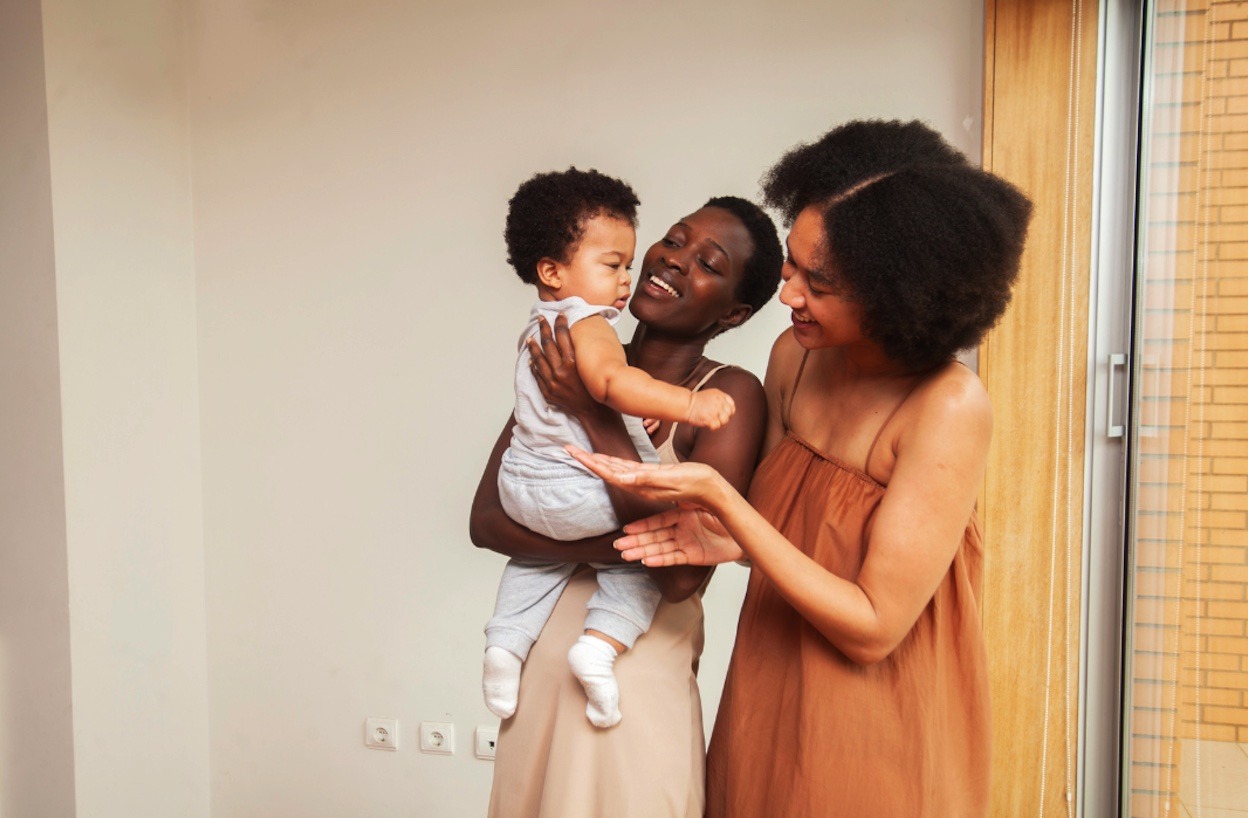 Two moms holding and smiling at their young infant.