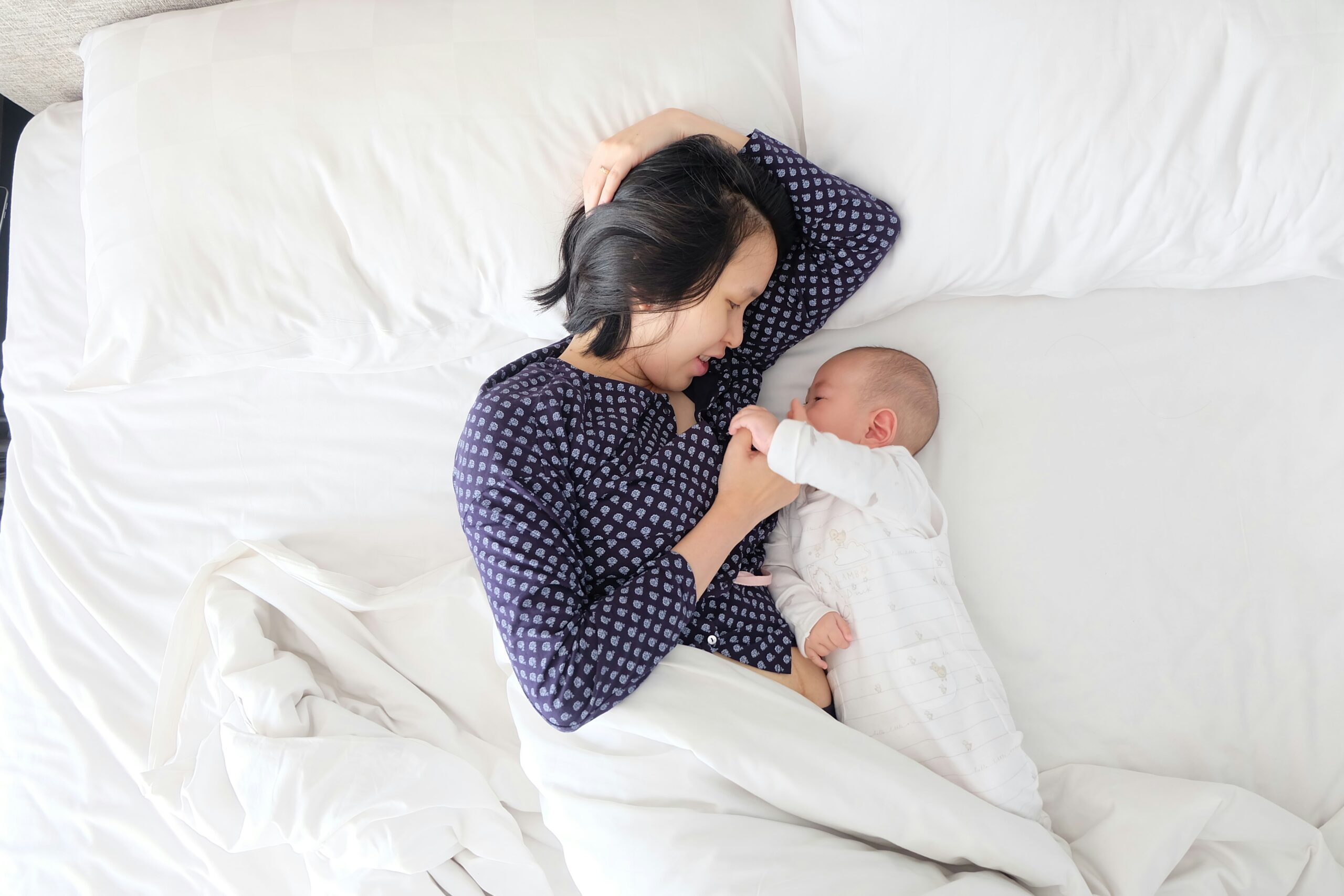 parent in bed resting, while feeding their baby in side-lying position.
